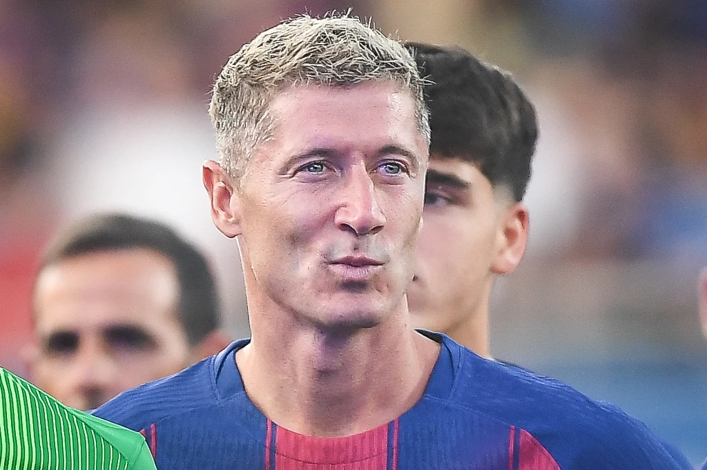 Mężczyzna w sportowej koszulce w niebiesko-czerwone pasy stoi w tłumie innych osób, wyróżnia się jasnymi, krótkimi włosami i skupioną miną.