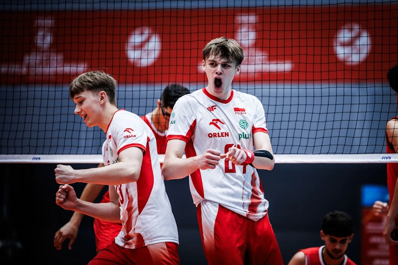 Siatkarze w biało-czerwonych strojach świętują punkt podczas meczu, wyrażając emocje i zaangażowanie na boisku, w tle widoczna siatka oraz fragmenty pozostałych zawodników.