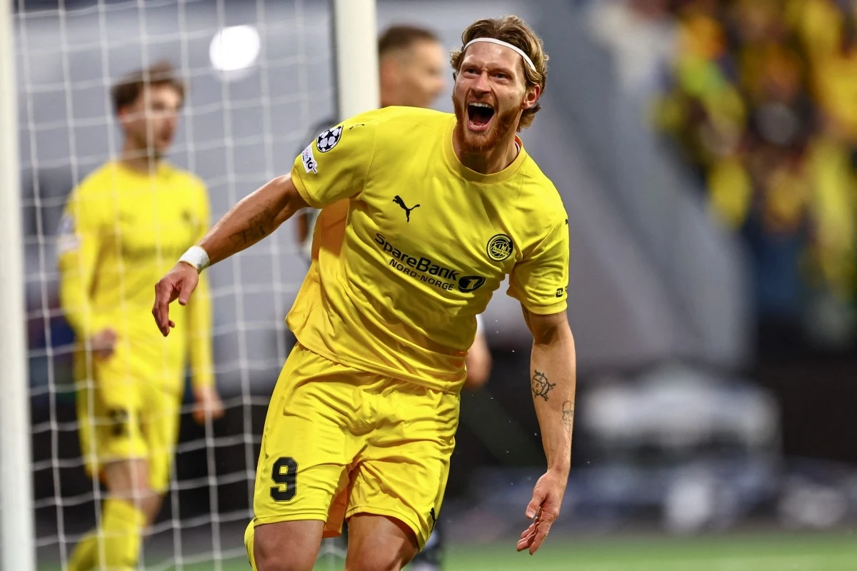 Piłkarz w żółtym stroju z numerem 9 świętuje zdobycie bramki, energicznie rozkładając ręce, w tle siatka bramki i inni zawodnicy.