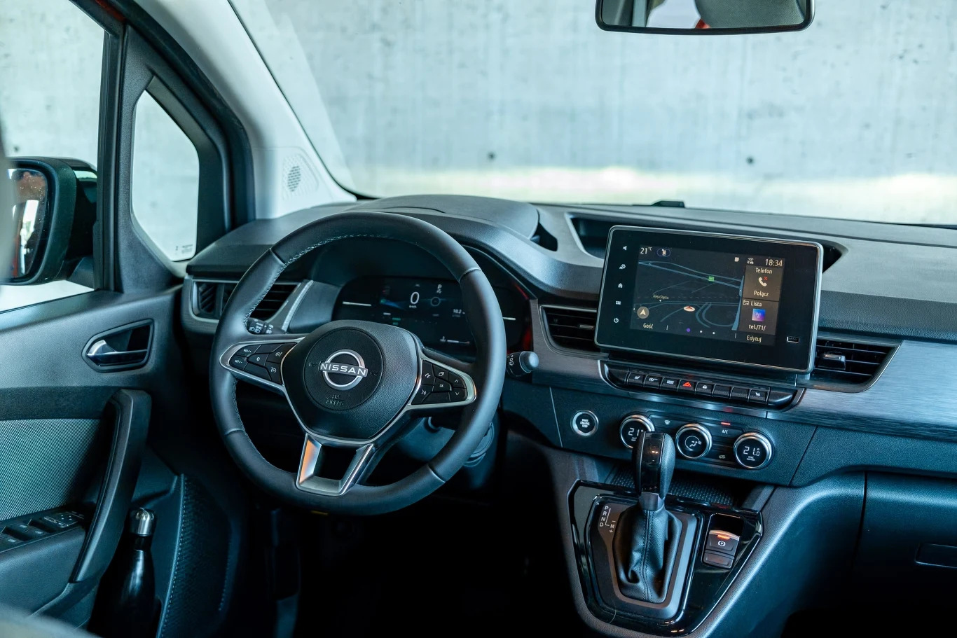Nowoczesna deska rozdzielcza samochodu Nissan z wielofunkcyjną kierownicą, cyfrowym wyświetlaczem za kierownicą oraz dużym ekranem dotykowym na konsoli centralnej, otoczona wygodnymi siedzeniami i minimalistycznym designem wnętrza.