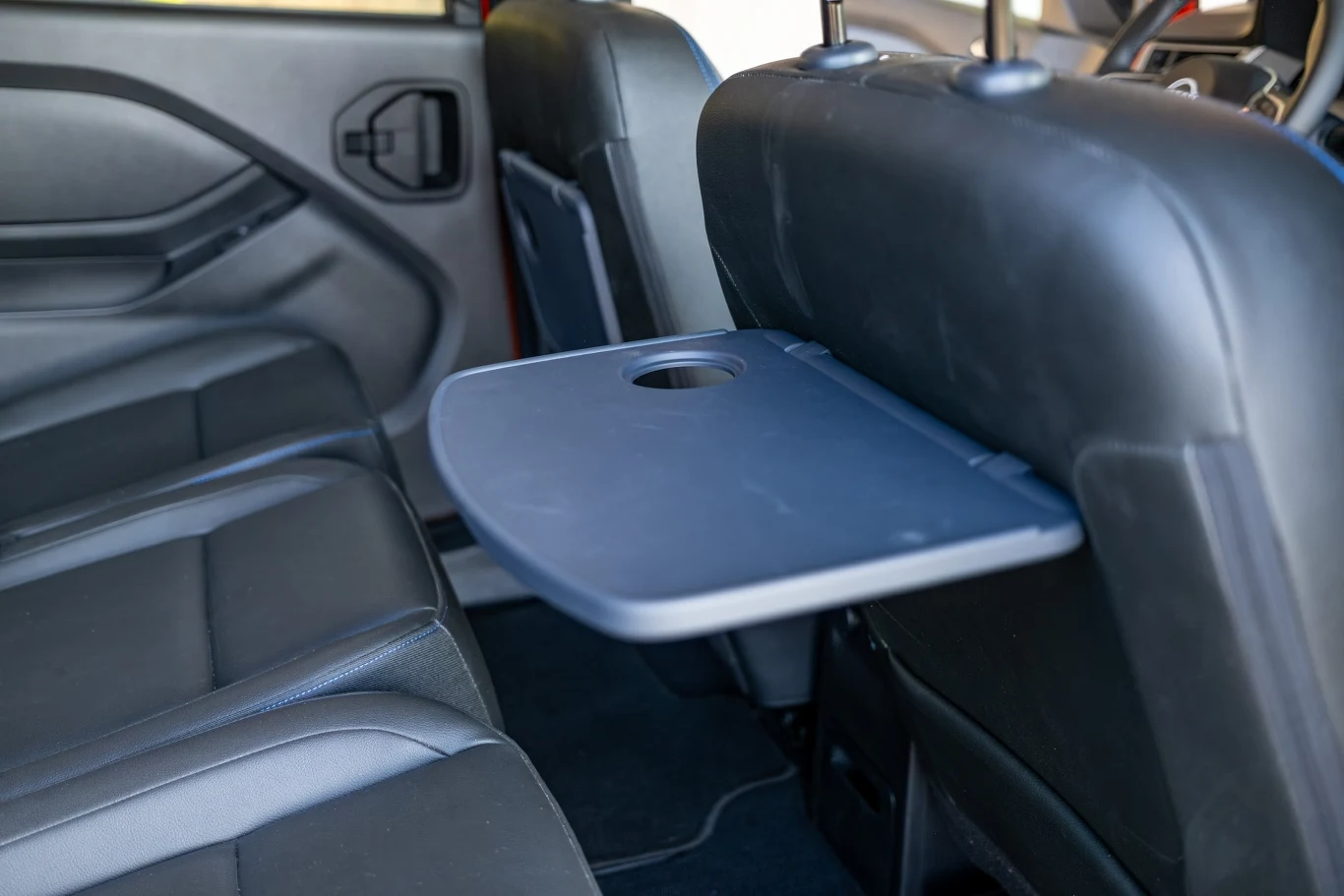 Tylna część samochodu z rozłożonym stolikiem zamontowanym z tyłu przedniego fotela, wokół skórzane siedzenia i przestrzeń do siedzenia pasażerów.