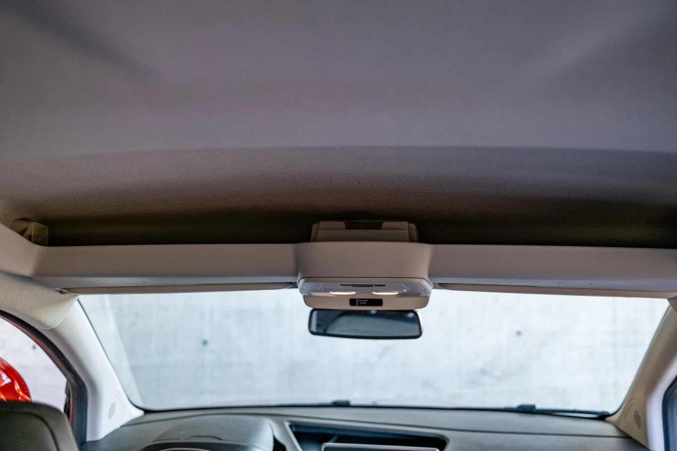 Wnętrze samochodu sfotografowane od tyłu, widoczny sufit, lusterko wsteczne i fragmenty przednich foteli.