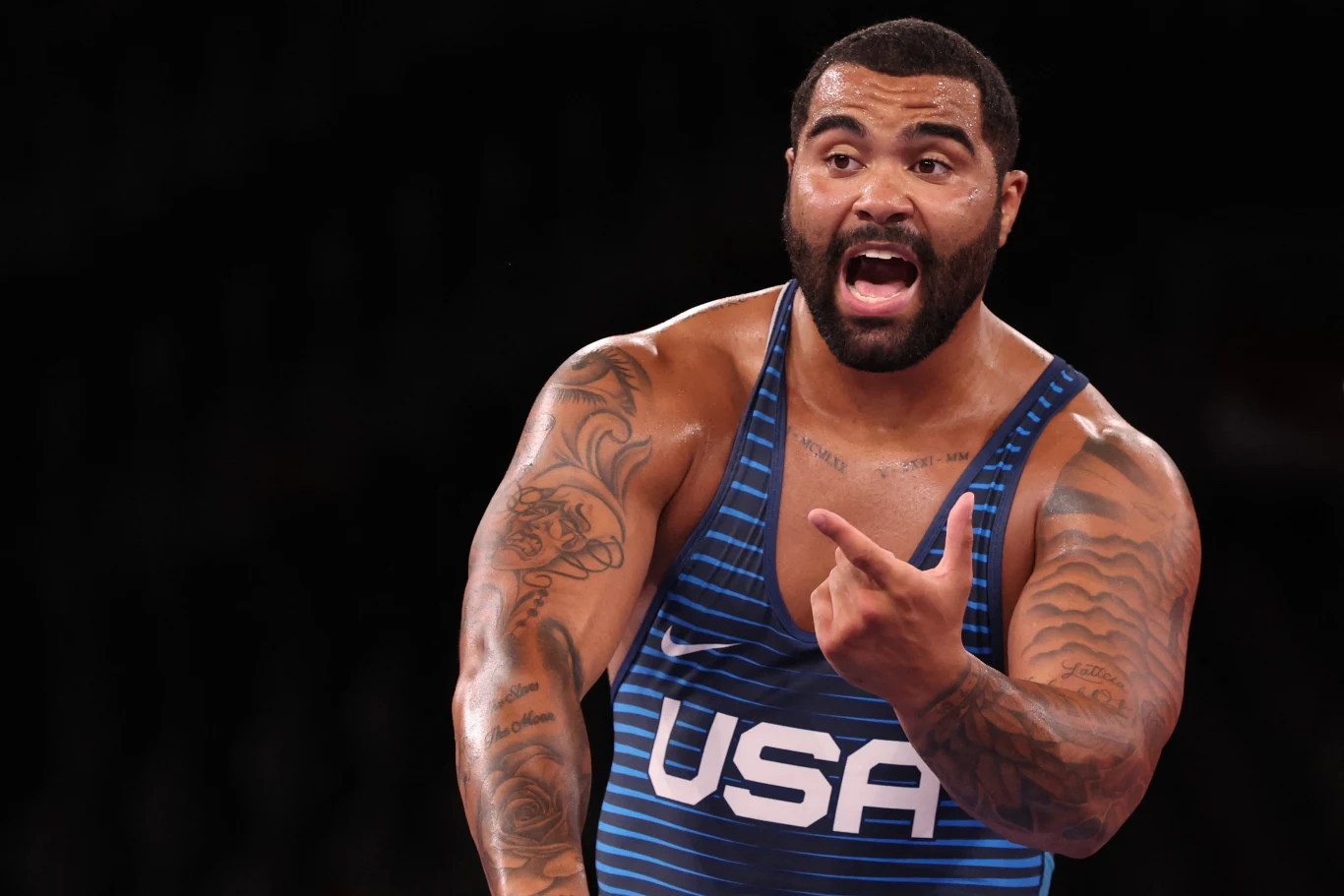 Gable Steveson Sportowiec w stroju z napisem USA gestykuluje i wyraża emocje podczas rywalizacji, widoczne są liczne tatuaże na ramionach.