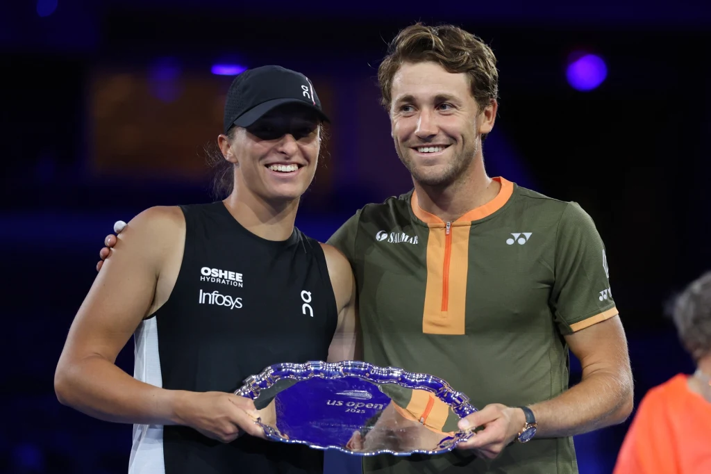 Iga Świątek i Casper Ruud Dwoje tenisistów pozuje razem z trofeum na tle ciemnego, podświetlonego stadionu, oboje uśmiechnięci i ubrani w sportowe stroje, jeden z nich trzyma dużą, srebrną tacę.