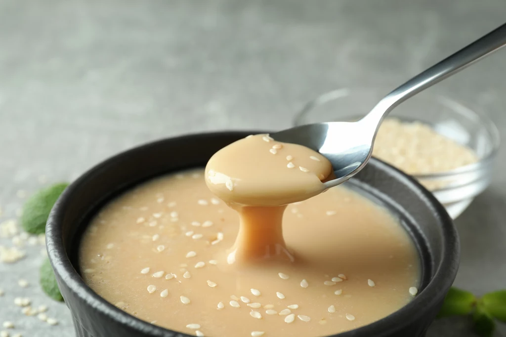 Sezam i pasta tahini są bardzo zdrowe i warto je jeść na co dzień, jednak chałwa – przez dużą ilość cukru – powinna pozostać tylko okazjonalnym deserem Gęsta pasta sezamowa w miseczce, posypana ziarnami sezamu, z łyżką nabierającą porcję pasty.