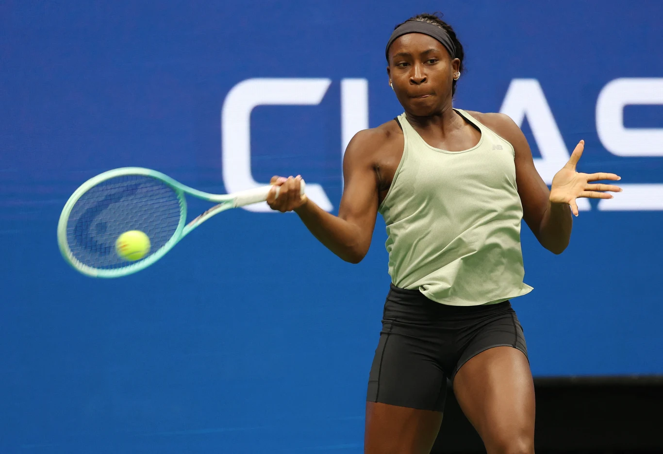 Coco Gauff Tenisistka w zielonym topie i czarnych szortach uderzająca piłkę podczas meczu na tle niebieskiego kortu.