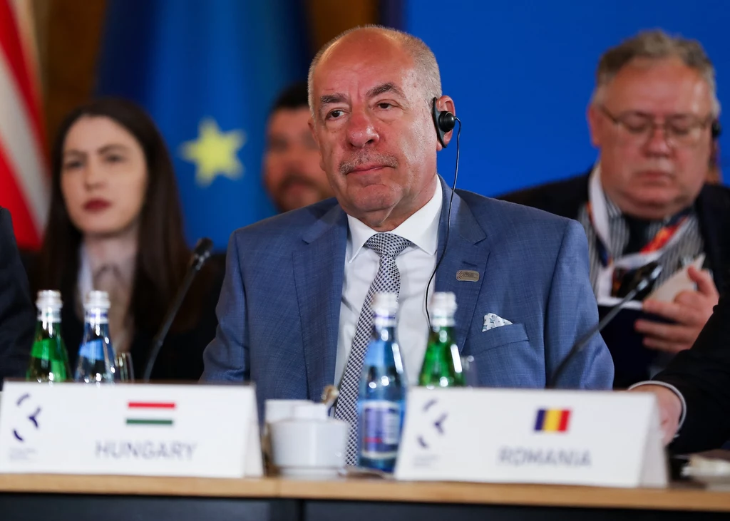 Węgierski prezydent Tamas Sulyok Mężczyzna w garniturze siedzi przy stole konferencyjnym z tabliczką "Hungary" oraz słuchawką do tłumaczenia, w tle osoby uczestniczące w spotkaniu oraz flagi Unii Europejskiej.