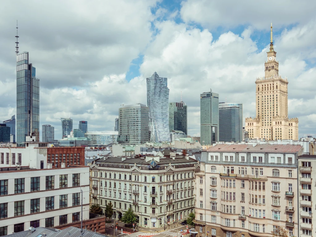Panorama centrum Warszawy z widokiem na wieżowce, Pałac Kultury i Nauki oraz zabytkowe kamienice w kontrastującym otoczeniu nowoczesnej zabudowy.