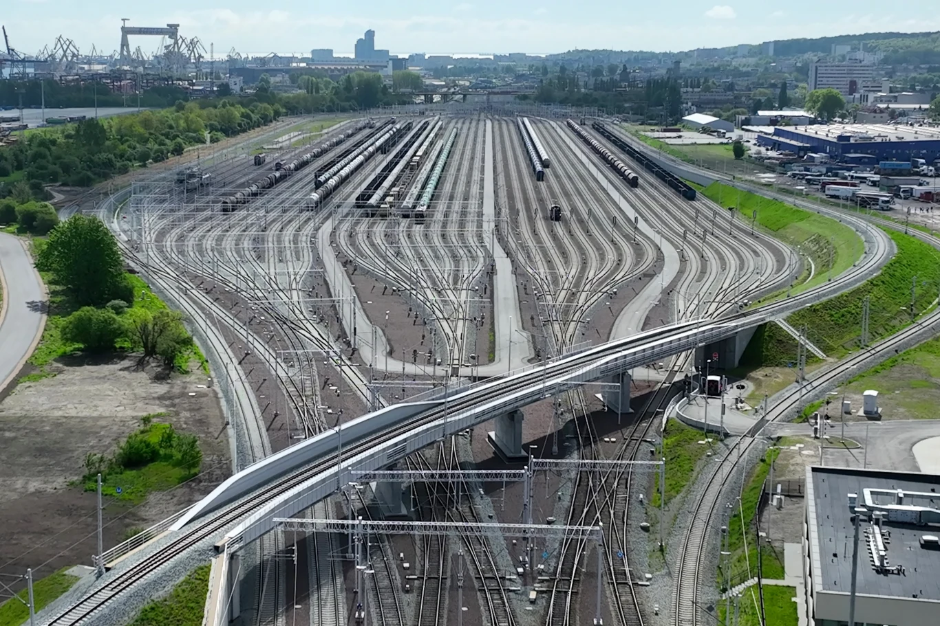 „Autostrada dla pociągów” to nowoczesna stacja kolejowa w Gdyni | Fot. PKP PLK SA Rozległy węzeł kolejowy z licznymi torami i zwrotnicami, pociągi towarowe stojące na torach, wiadukt nad torami i przemysłowa infrastruktura w tle.