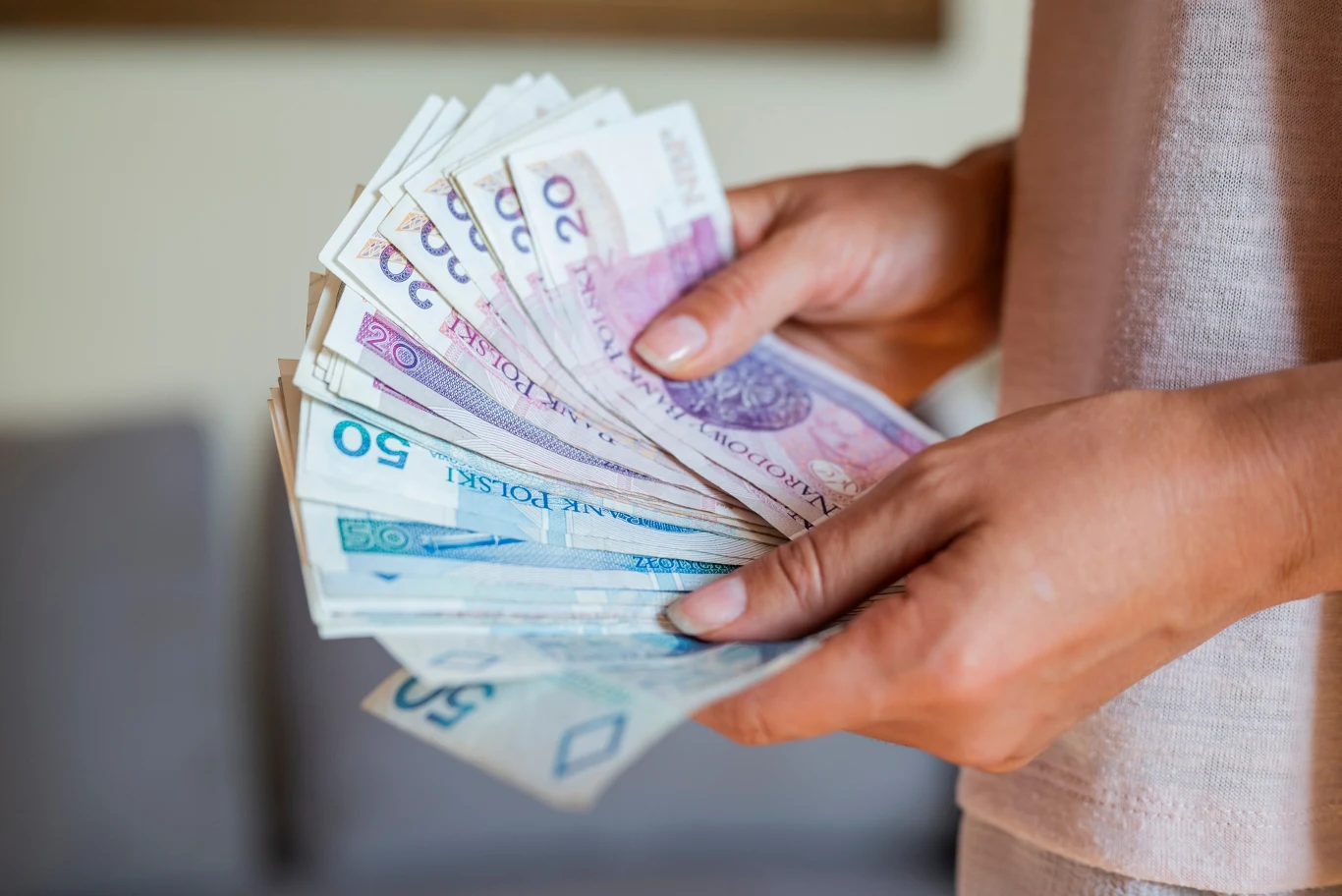 Ręce trzymające plik polskich banknotów o różnych nominałach, skupienie na gotówce i dłoniach.