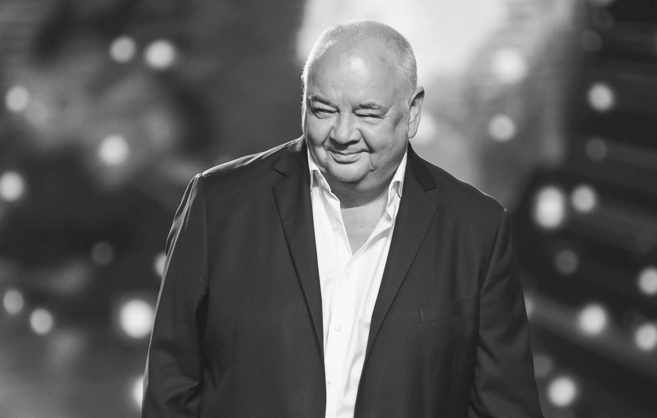 Są nowe doniesienia w sprawie śmierci Stanisława Soyki Uśmiechnięty mężczyzna w średnim wieku w eleganckim garniturze na tle rozmytego, jasnego, scenicznego światła.