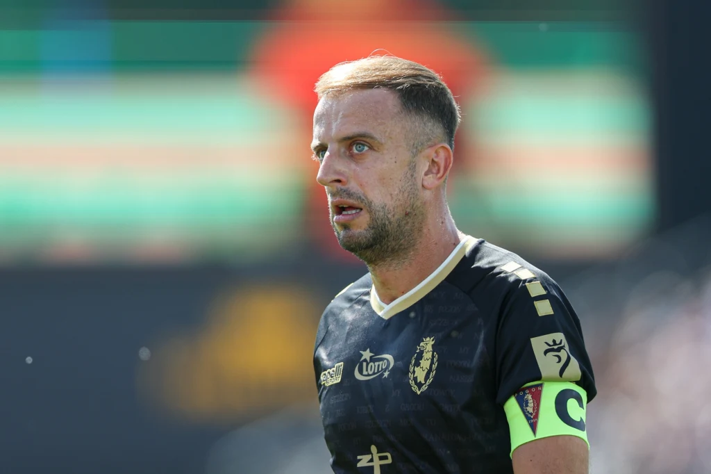 Kamil Grosicki był jednym z bohaterów Pogoni Szczecin w spotkaniu z Cracovią Piłkarz w ciemnej koszulce z opaską kapitańską na ramieniu skupiony patrzy przed siebie podczas meczu, w tle rozmazane barwy trybun.
