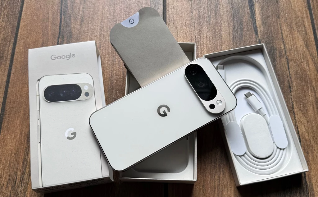 Zawartość opakowania z Google Pixel 10 Pro. Nowy biały smartfon Google Pixel wraz z pudełkiem, widocznym kablem do ładowania USB oraz dokumentacją, całość ułożona na drewnianej powierzchni