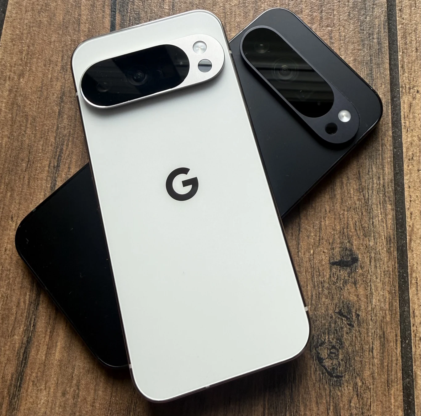 Dwa nowoczesne smartfony Google Pixel w kolorze białym i czarnym ułożone na drewnianym blacie, z widocznymi charakterystycznymi aparatami fotograficznymi oraz logo G pośrodku tylnej obudowy.