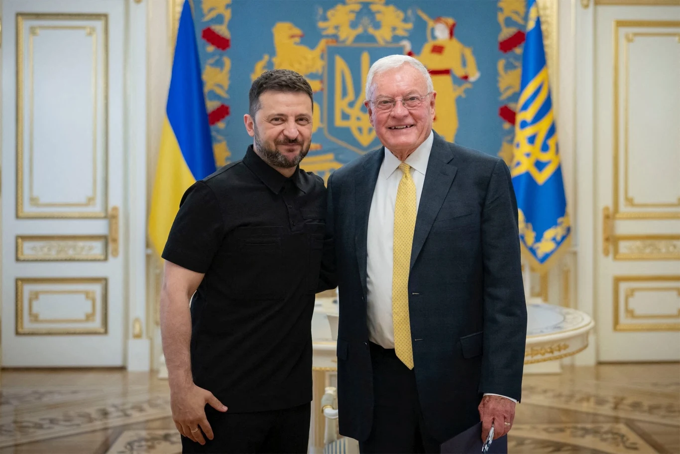 Wołodymyr Zełenski odznaczył Keitha Kellogga Dwóch mężczyzn stoi obok siebie w eleganckim wnętrzu, za nimi widoczne są ukraińskie flagi oraz herb państwowy na tle dekoracyjnych drzwi.