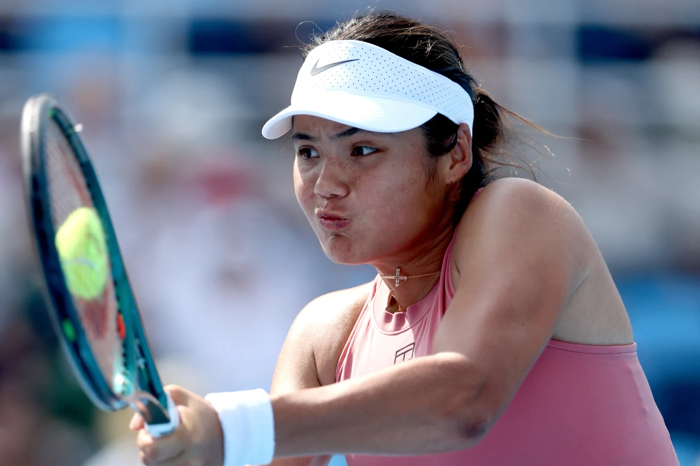 Emma Raducanu Tenisistka w różowym stroju sportowym w trakcie dynamicznego uderzenia piłki rakietą, skupiona na grze, z białą opaską na głowie, na tle nieostrego trybuny.