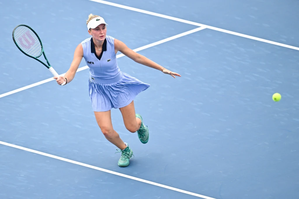 Tenisistka w niebieskiej sukience podczas gry na kortach twardych, biegnąca w kierunku piłki, skoncentrowana na odbiciu, w dynamicznej pozie.