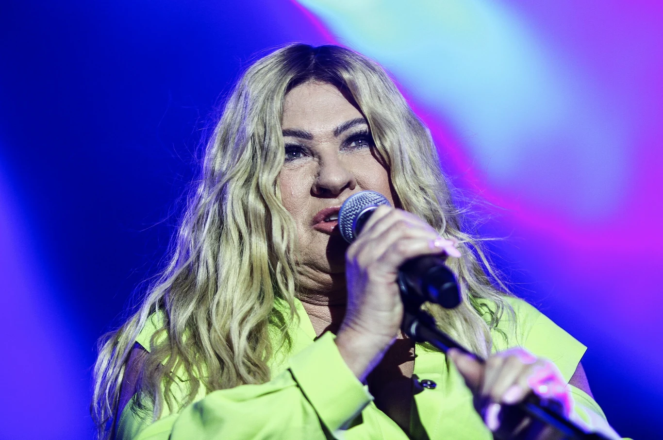 Beata Kozidrak powróciła na scenę po walce z chorobą Kobieta o długich blond włosach występuje na scenie z mikrofonem w ręku, ubrana w jasnożółtą koszulę, na tle kolorowego, rozmytego oświetlenia.