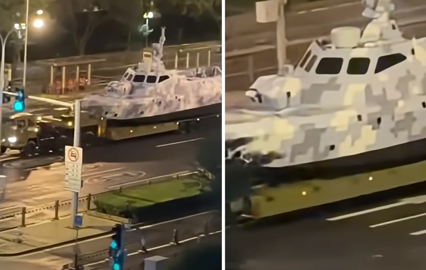 Nowy dron morski chińskiej marynarki. "Debiutuje" podczas prób przed paradą wojskową w stolicy Mały okręt wojskowy w kamuflażu transportowany na specjalnej platformie przez miejską ulicę nocą, oświetlenie uliczne, widoczna infrastruktura miejska i zieleń w tle.