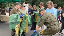 Grupa osób, w tym żołnierze w mundurach oraz wolontariusze, segreguje śmieci do kolorowych worków na świeżym powietrzu podczas akcji ekologicznej.