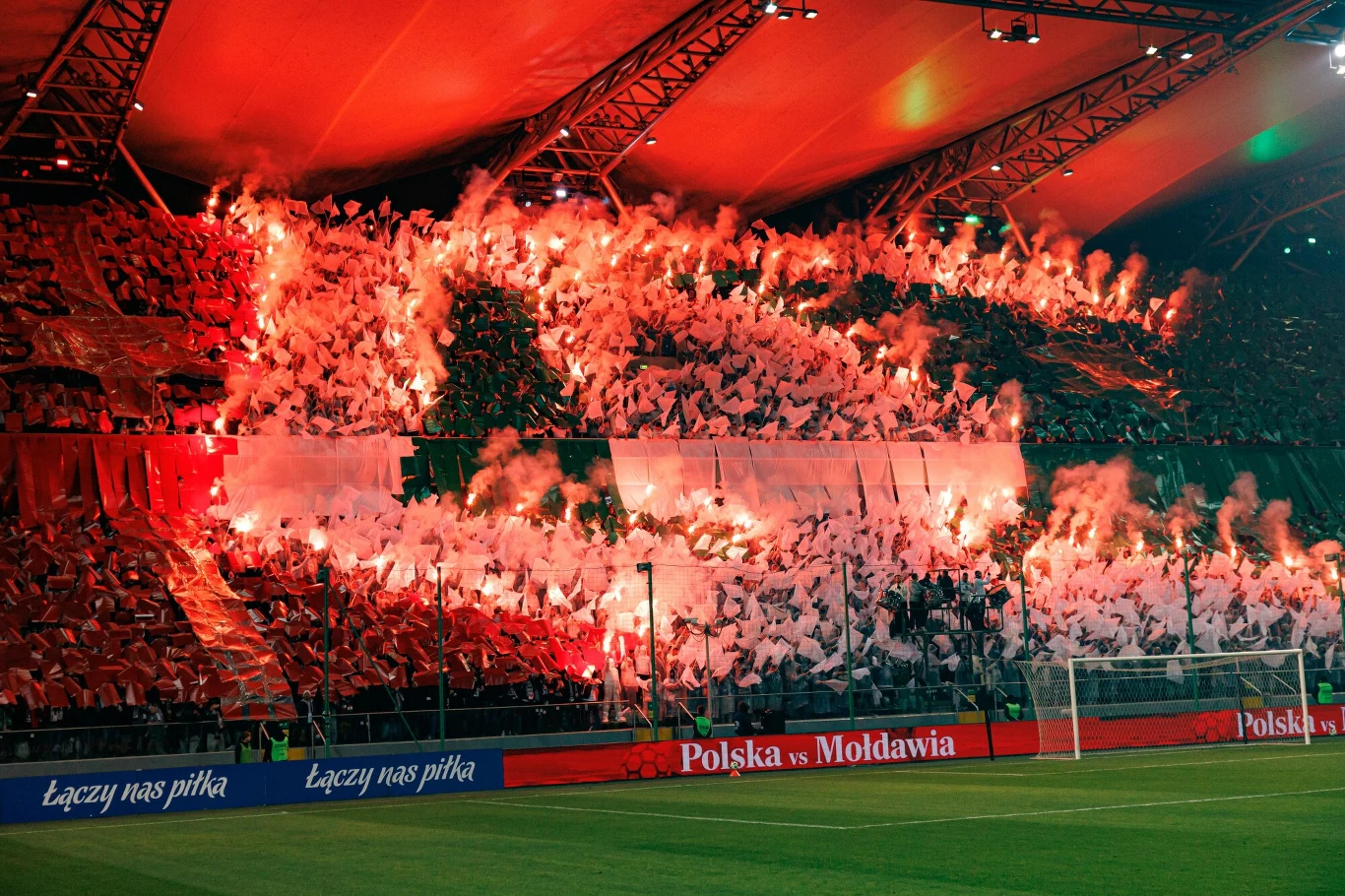 Stadion Legii Warszawa Tłum kibiców na stadionie piłkarskim trzyma flagi i odpala race świetlne, tworząc efektowną i intensywną oprawę podczas meczu Polska vs Mołdawia.