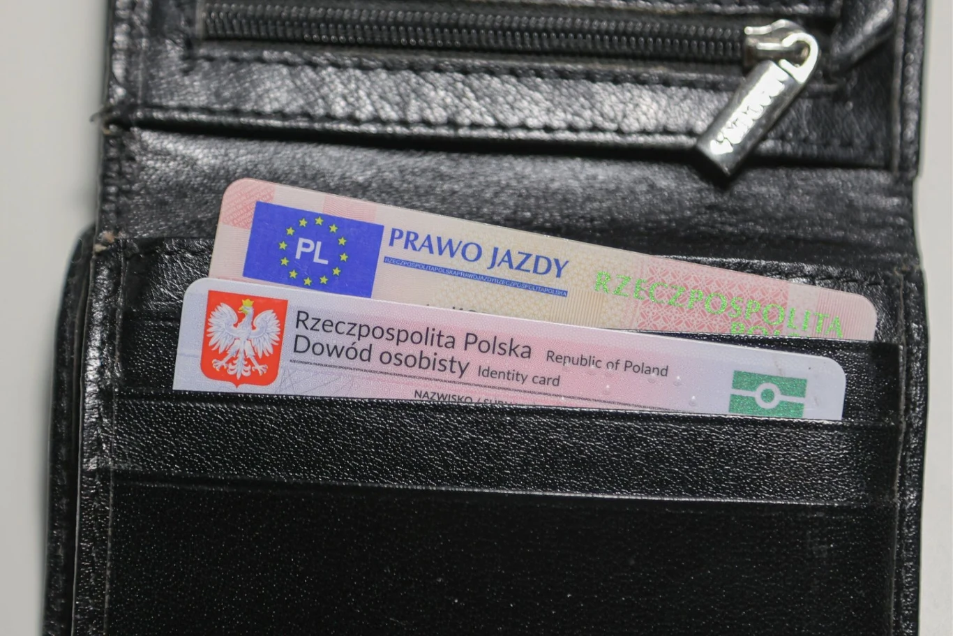 Ile kosztuje wydanie prawa jazdy i dowodu rejestracyjnego w 2026 roku? Portfel wykonany z czarnej skóry z widocznymi dwoma dokumentami: polskim dowodem osobistym i prawem jazdy, wsuniętymi w wewnętrzną kieszeń.