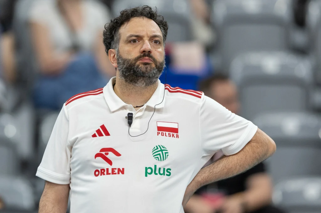 Stefano Lavarini Mężczyzna z brodą w koszulce reprezentacji Polski z logotypami sponsorów, stojący ze zgiętą ręką na biodrze w hali sportowej; w tle rozmyte sylwetki osób i trybuny.