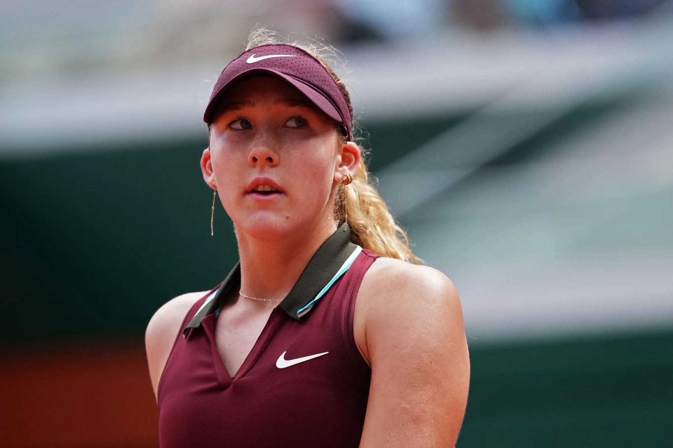 Młoda kobieta w sportowej odzieży tenisowej i bordowej czapce z daszkiem na korcie tenisowym, skupiona podczas meczu.