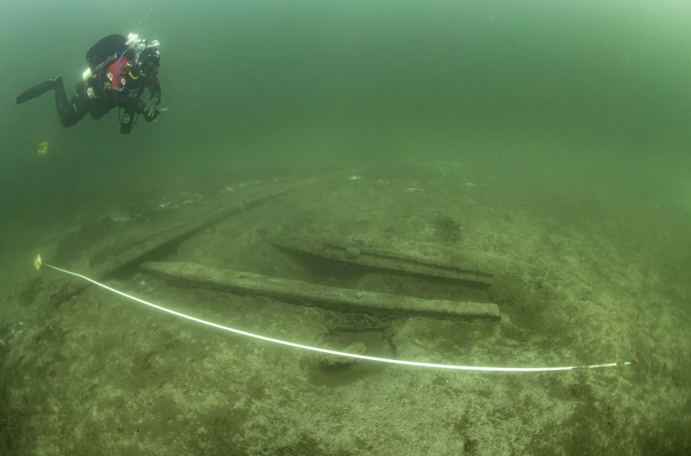 Badania archeologiczne wraku z XV wieku ujawniły detale na temat doskonale zachowanej okrętowej artylerii. Nurek prowadzi badania podwodnej konstrukcji z drewnianych belek, oznaczonych taśmą pomiarową, w zielonkawej wodzie.
