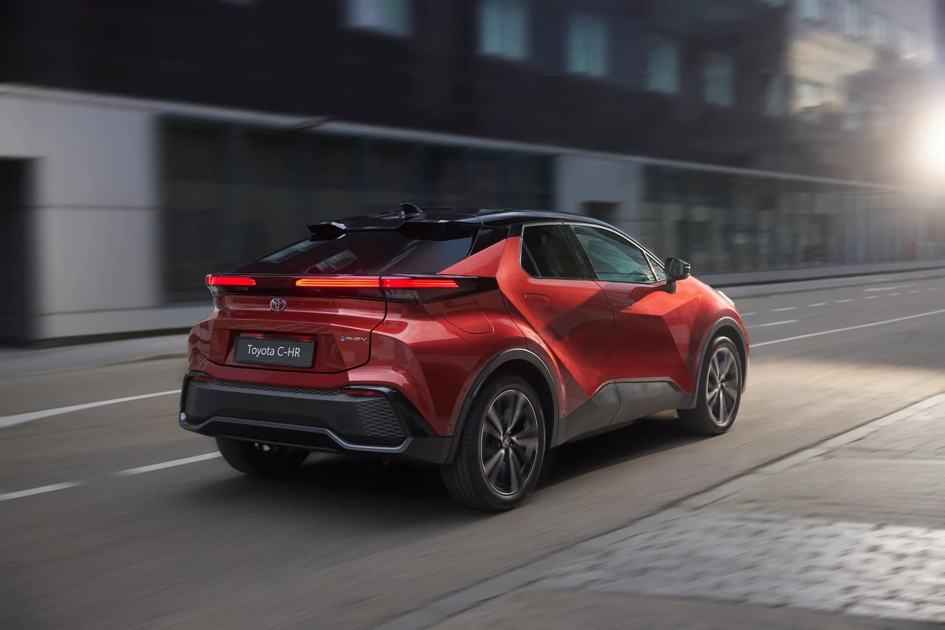 Toyota C-HR Czerwony samochód Toyota C-HR podczas jazdy pustą miejską ulicą, dynamiczne światło podkreśla nowoczesny design pojazdu