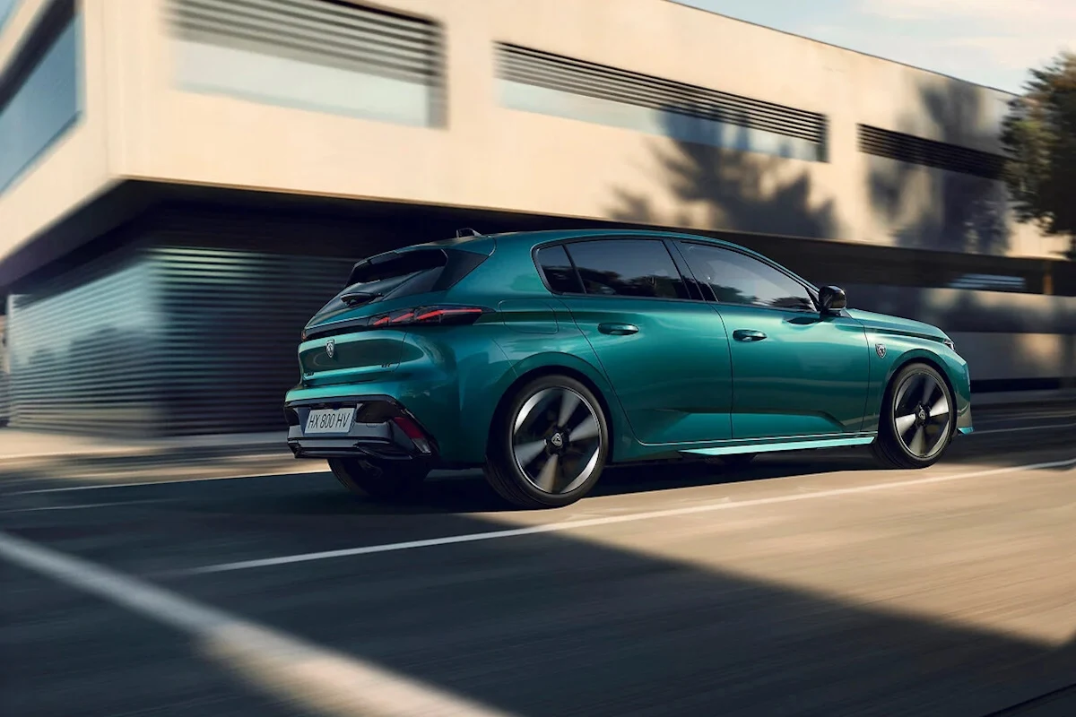 Peugeot 308 po liftingu Nowoczesny, zielony samochód osobowy poruszający się po miejskiej ulicy przy nowoczesnym budynku, w tle widać dynamiczne rozmazanie otoczenia podkreślające ruch pojazdu.