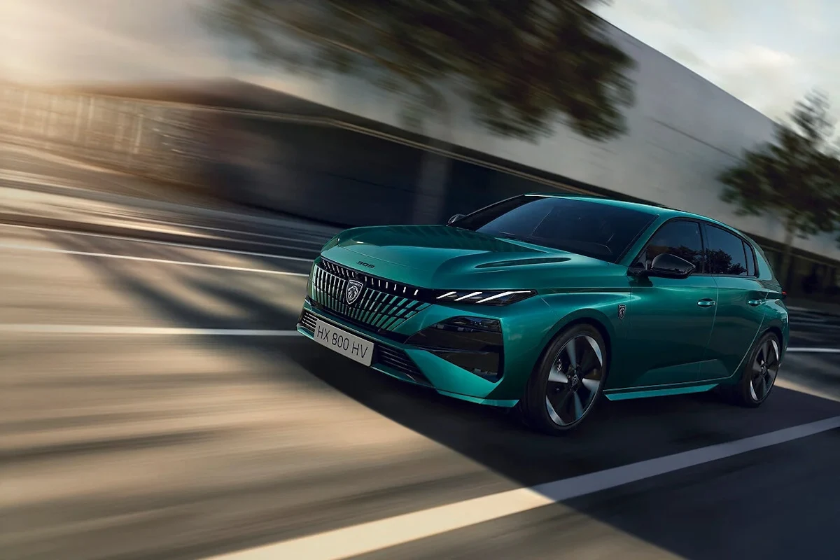 Peugeot 308 po liftingu w jednym z nowym lakierów Nowoczesny, turkusowy samochód osobowy porusza się miejską drogą, w tle rozmazane budynki oraz drzewa sugerujące ruch i dynamikę pojazdu.