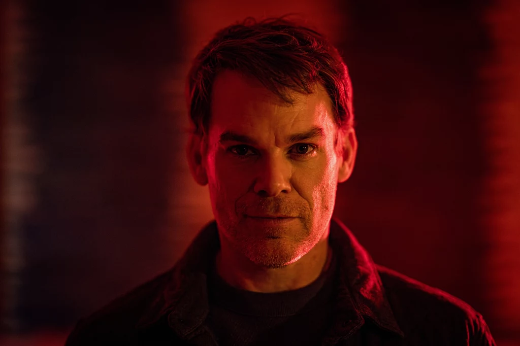 Jest Dexter, są emocje. W nowym serialu bohater będzie musiał się zmierzyć z demonami przeszłości. Portret mężczyzny w średnim wieku o poważnym wyrazie twarzy, oświetlony ciepłym, czerwonym światłem na tle rozmytego, ciemnego tła.