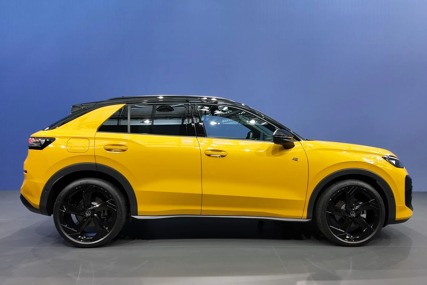 Nowoczesny żółty samochód typu SUV z czarnym dachem i lśniącymi, dużymi felgami stoi na neutralnym tle w dobrze oświetlonym pomieszczeniu.