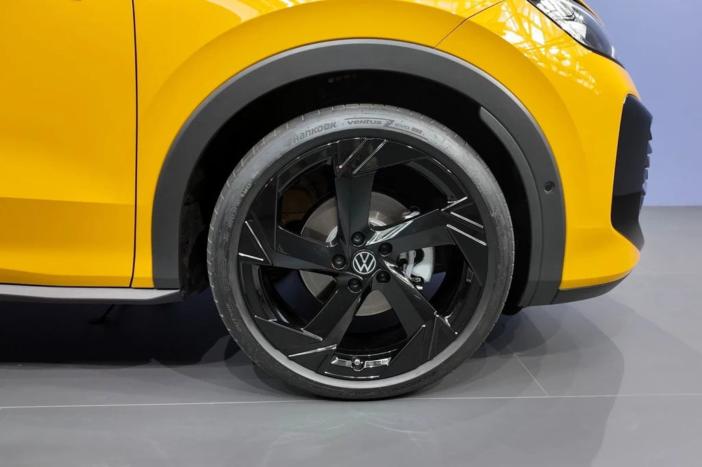 Nowy T-Roc będzie mógł stać nawet na 20-calowych kołach. W poprzedniej generacji maksymalnie można było dostać koła 19-calowe. Czarne aluminiowe felgi z logo Volkswagena zamontowane na przednim kole żółtego samochodu, widoczne detale karoserii oraz odbicia światła na lakierze.