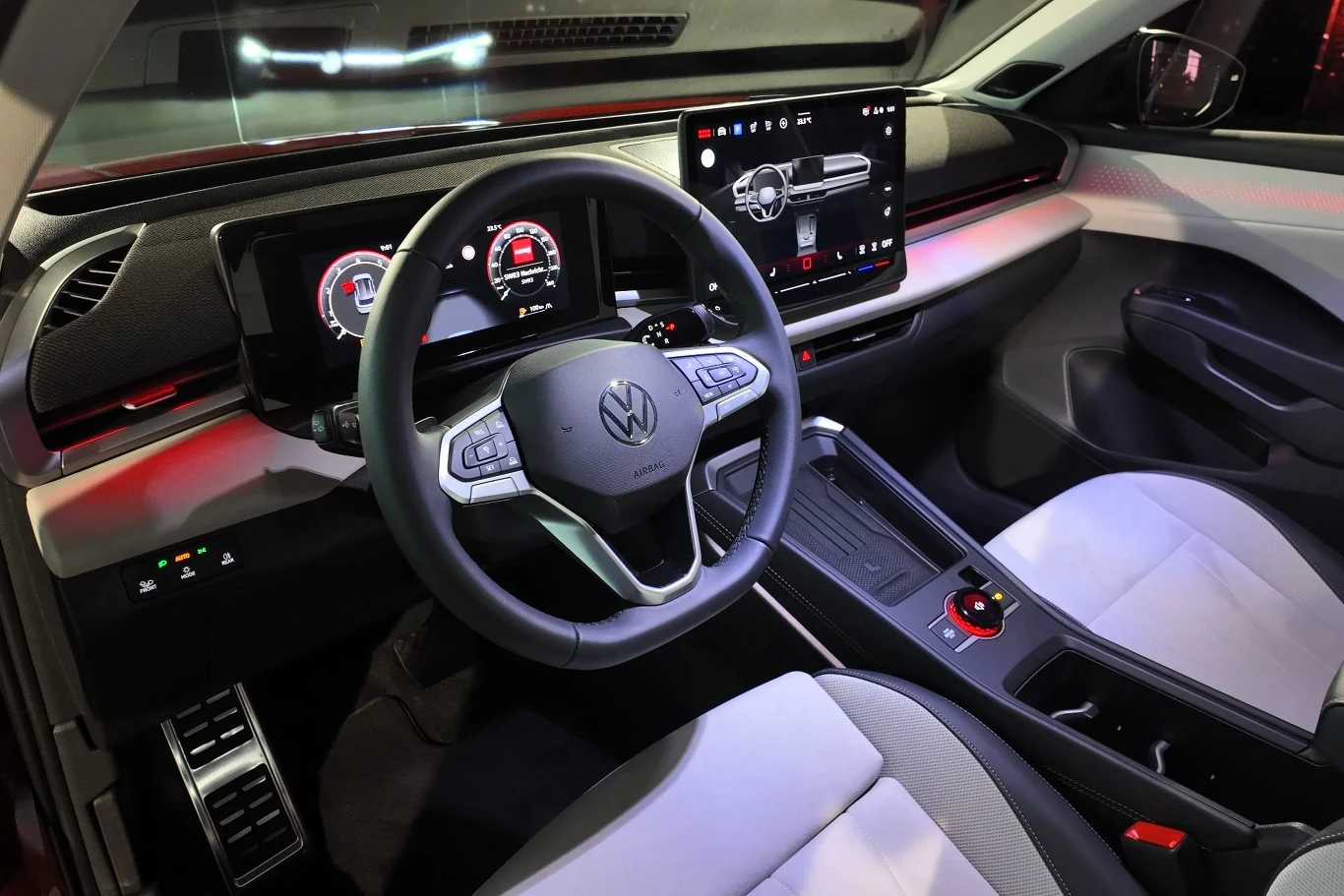 Kokpit nowoczesnego samochodu marki Volkswagen wyposażony w cyfrowe zegary, duży dotykowy ekran multimedialny, podświetlenie ambientowe i nowoczesną kierownicę z funkcjami sterowania dotykowego.