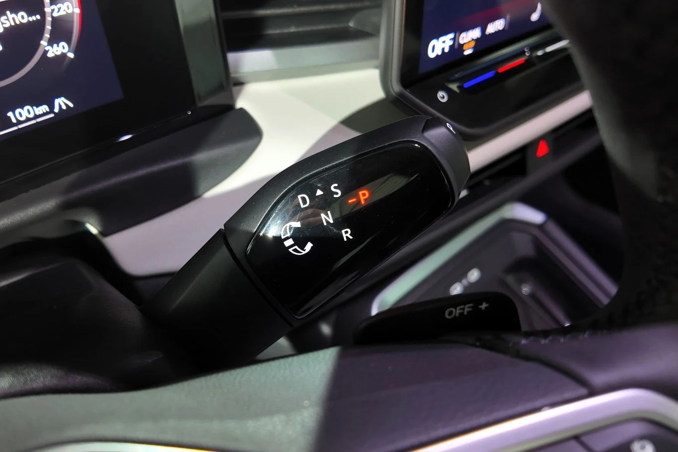 Dźwignia zmiany biegów automatycznej skrzyni biegów w nowoczesnym samochodzie otoczona elementami wnętrza, widoczne oznaczenia trybów jazdy i podświetlenie wskaźników.