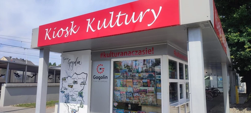 Kiosk promujący kulturę z czerwonym szyldem Kiosk Kultury, na ścianie mapa regionu Gogolin oraz liczne materiały informacyjne i broszury widoczne przez szybę.