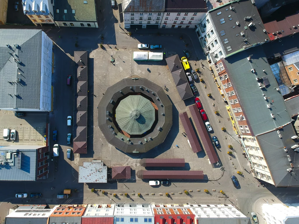 Krakowski Kazimierz. Plac Nowy z lotu ptaka Widok z lotu ptaka na charakterystyczny, ośmiokątny budynek otoczony mniejszymi zabudowaniami i ulicami z zaparkowanymi samochodami w centrum miasta.