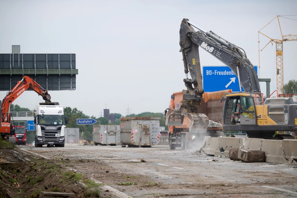 Po 10 latach rusza budowa autostrady A20 w Niemczech. | Fot. ilustracyjna Ciężkie maszyny budowlane pracujące nad remontem drogi, betonowe bariery oraz znak kierunkowy wskazujący zjazd na BO-Freudenberg, widoczna infrastruktura drogowa i budowlana tło podkreślają charakter robót.
