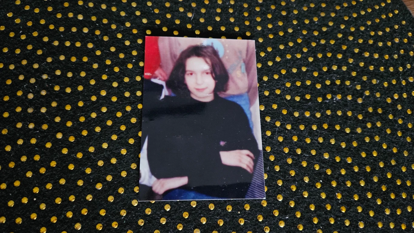 Jedno z nieliczonych zdjęć Basi Portret młodej osoby o jasnej karnacji i ciemnych włosach, ubranej na czarno, siedzącej z lekko skrzyżowanymi ramionami, sfotografowanej na tle wzorzystego materiału w czarne i żółte kropki.