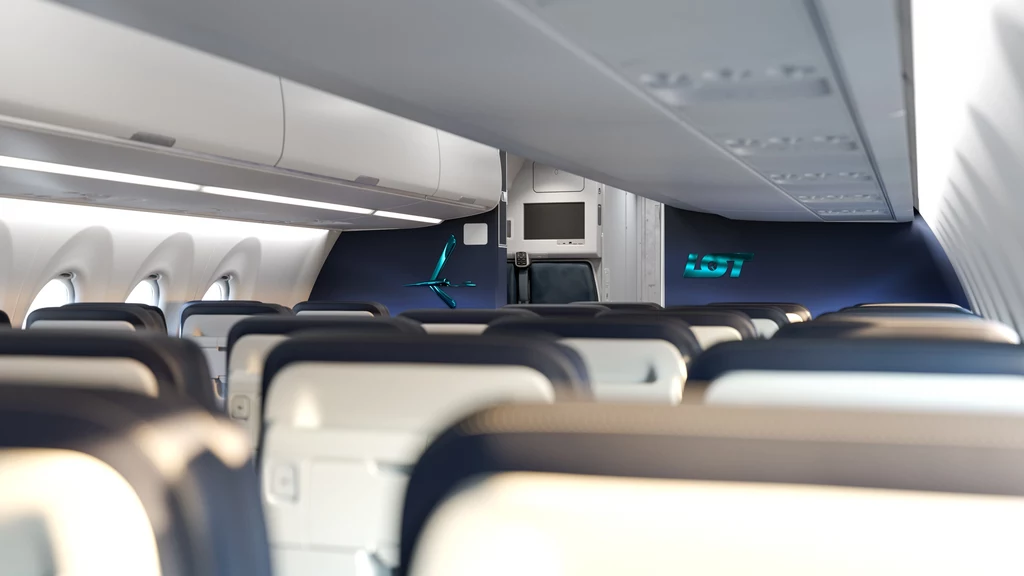 Fotele do lotowskich Airbusów A220 będą produkowane w fabryce RECARO w Świebodzinie. Puste wnętrze samolotu pasażerskiego z widocznymi rzędami siedzeń, oknami po lewej stronie oraz oświetleniem LED wzdłuż schowków bagażowych. Airbus A220 LOT