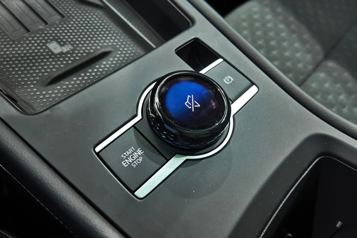 Centralny panel sterowania w samochodzie ze szczegółowym widokiem pokrętła z ikoną wyciszenia dźwięku, przyciskiem start/stop silnika oraz przyciskiem hamulca ręcznego elektronicznego.