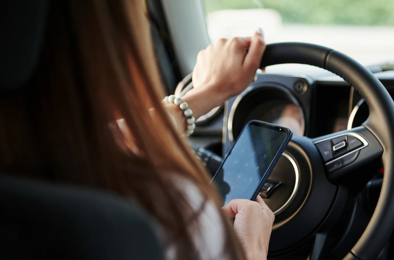 Jak uniknąć mandatu za prędkość dzięki Google Maps? Osoba prowadzi samochód jedną ręką, a w drugiej trzyma smartfon, skupiając uwagę na ekranie telefonu zamiast na jeździe.