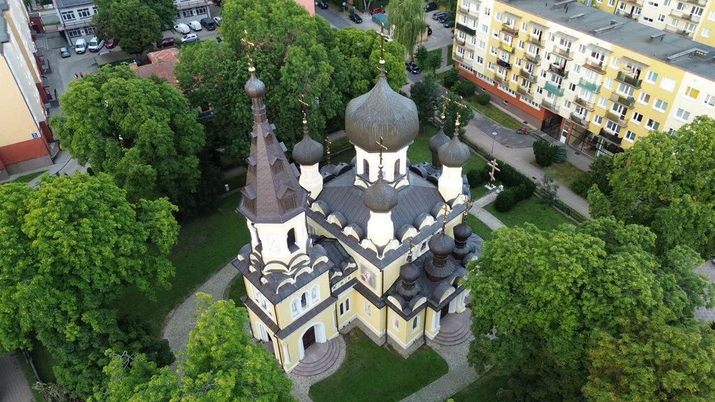 Cerkiew z charakterystycznymi cebulastymi kopułami w otoczeniu drzew i sąsiadujących bloków mieszkalnych, widok z lotu ptaka