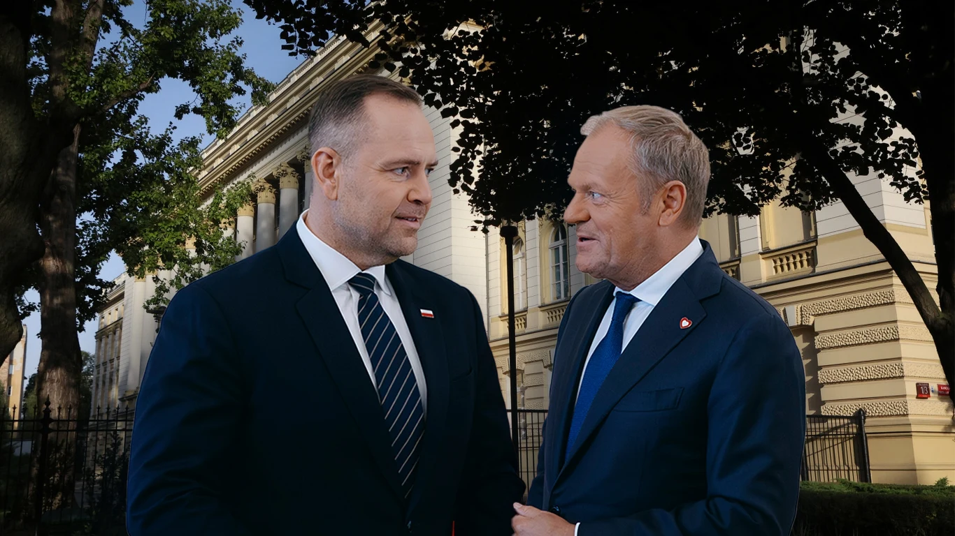 Dwóch mężczyzn w garniturach rozmawia ze sobą na tle zabytkowego budynku, obaj mają przypinki z flagą Polski na klapach marynarek.