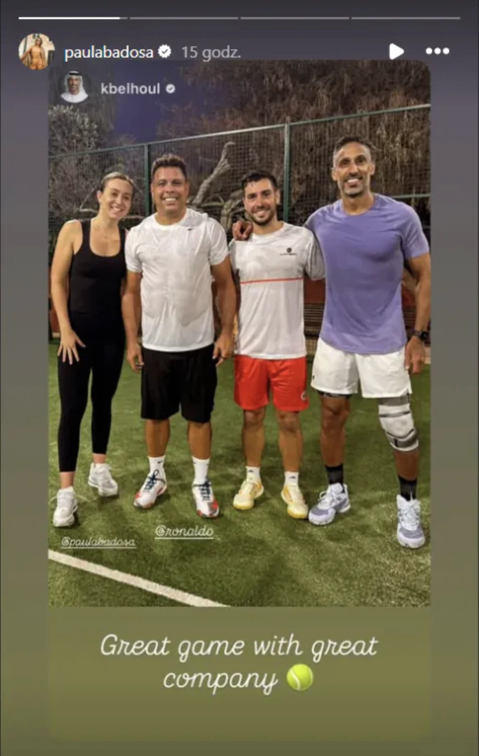 Czworo dorosłych stoi razem na korcie tenisowym wieczorem, uśmiechając się i ubranych w stroje sportowe, trzymając się blisko siebie po wspólnej grze.