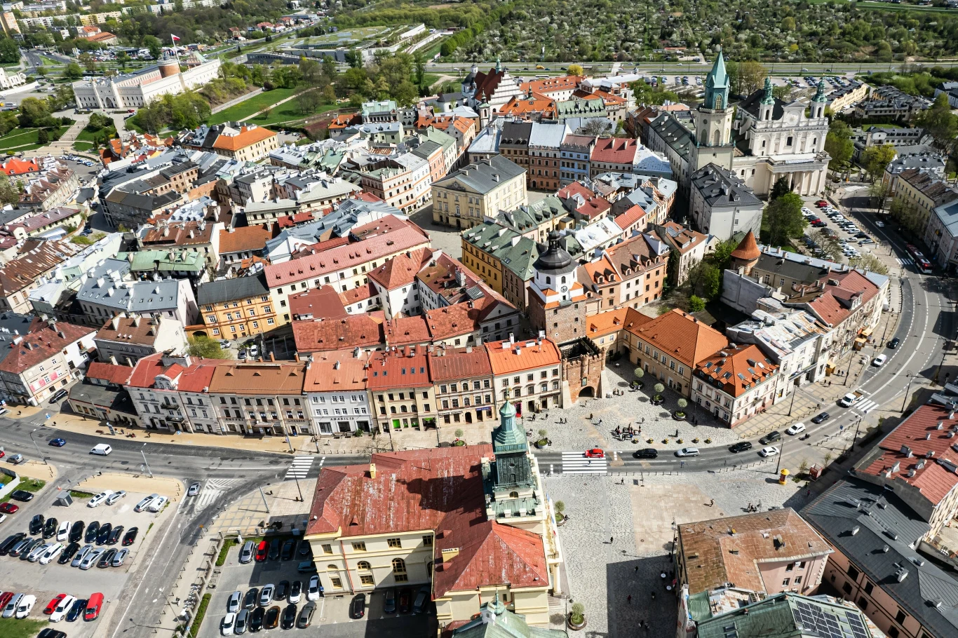 Stare Miasto w Lublinie - Brama Krakowska, Plac Króla Władysława Łokietka, Ratusz Miasta Lublin, Archikatedra św. Jana Chrzciciela i św. Jana Ewangelisty Panorama historycznego centrum miasta z charakterystyczną zabudową, licznymi kamienicami, kościołem oraz brukowanymi uliczkami otoczoną zielenią i parkingiem samochodowym.