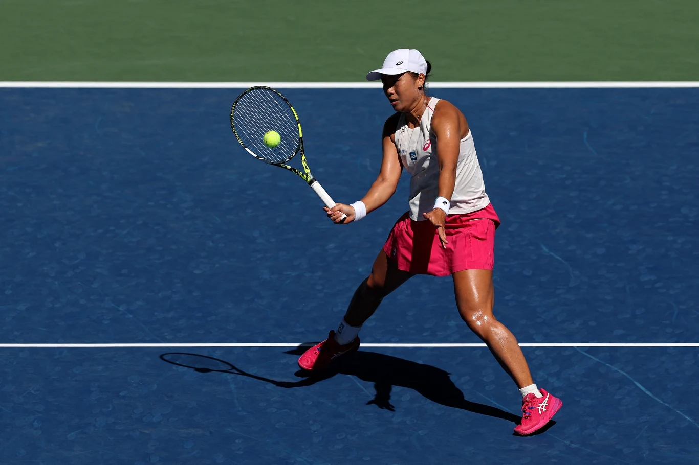 Tenisistka w sportowym stroju podczas rozgrywki, wykonuje uderzenie rakietą w kierunku nadlatującej piłki tenisowej na niebieskim korcie.