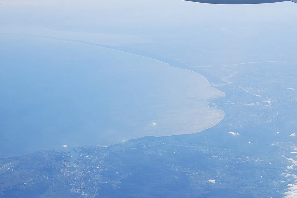 Głębia Gdańska to najgłębszy punkt u wybrzeży Polski. Znajduje się w rejonie Zatoki Gdańskiej. Widok na linię brzegową oraz ujście rzeki do morza, z lekką mgłą nad wodą i fragmentami chmur, fotografowane z perspektywy lotu samolotem.